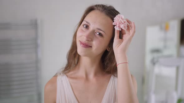 Portrait of Happy Young Slim Woman in Wedding Dress Putting Pink Flower in Hair Smiling Looking at alt