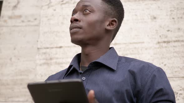 Young black american man using digital tablet in the street and looking around  alt