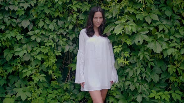 Female Model in White Tunic Dress with Green Leaves on Background alt