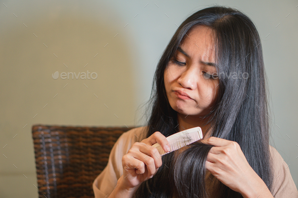 Unhappy lady brushing her dry messy hair with problem hair, Thin hair porblem.