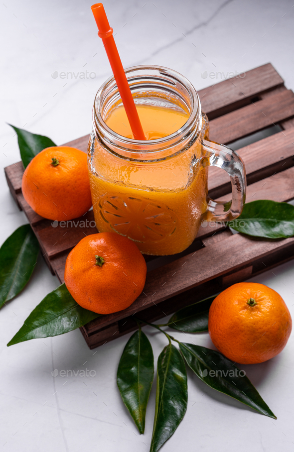 Closeup of fresh mandarin juice in a glass jar with a plastic reusable  straw on a wooden tray Stock Photo by wirestock