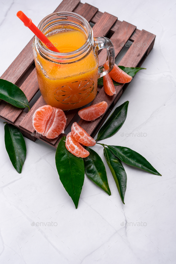 Closeup of fresh mandarin juice in a glass jar with a plastic reusable  straw on a wooden tray Stock Photo by wirestock