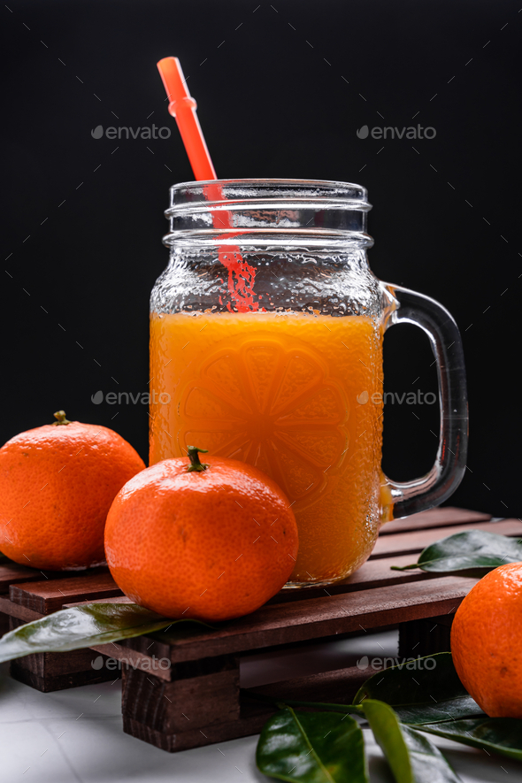 Closeup of fresh mandarin juice in a glass jar with a plastic reusable  straw on a wooden tray Stock Photo by wirestock