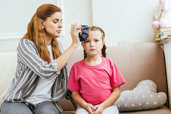 worried mom holding ice bag compress on head of daughter with headache