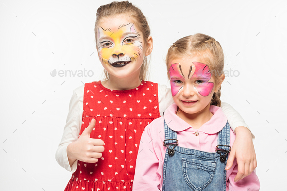 adorable kid with cat muzzle painting on face showing thumb up while embracing friend with painted