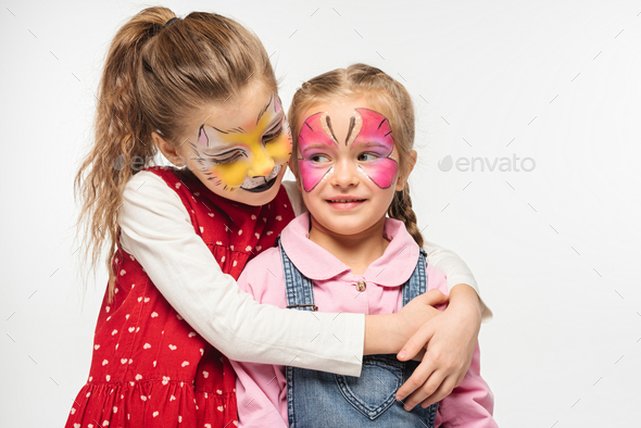 adorable kid with cat muzzle painting on face embracing friend with painted butterfly mask isolated