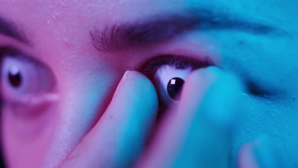 Closeup of a Browneyed Young Woman Taking Off the White Decorative Lens with Fingers in Ultraviolet alt