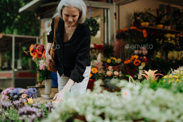 Portrait of a beautiful mature woman shopping at fresh flowers market ...