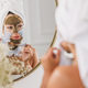 Woman In Front Of Mirror Removing Facial Mask In The Bathroom At Home - PhotoDune Item for Sale