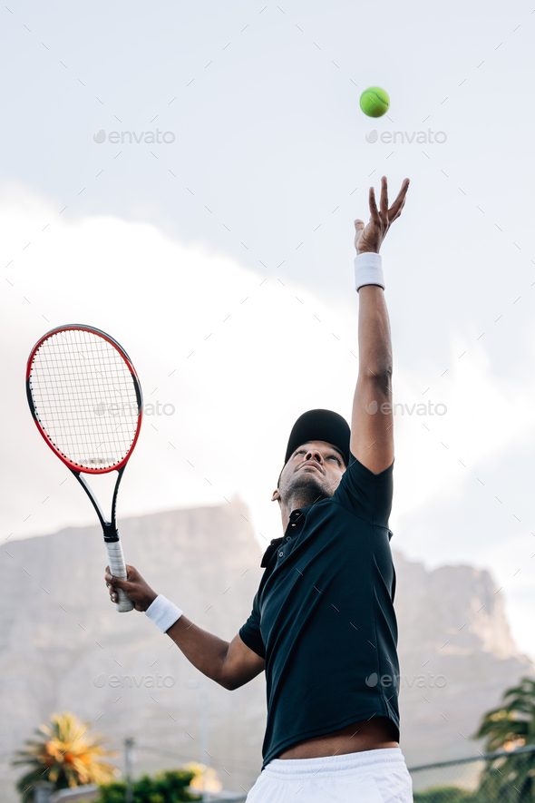 Tennis player throwing a ball in the air hitting a serve. Player is