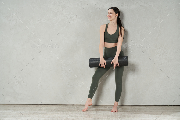 Young slim female in sports top and leggings standing barefoot on