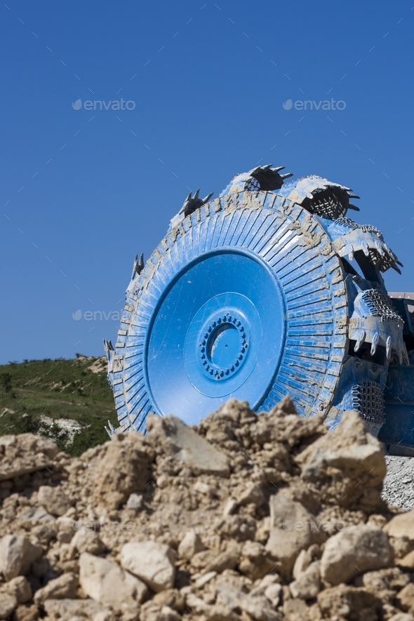 Vertical closeup shot of a blue rotary wheel excavator in a quarry under the clear sky