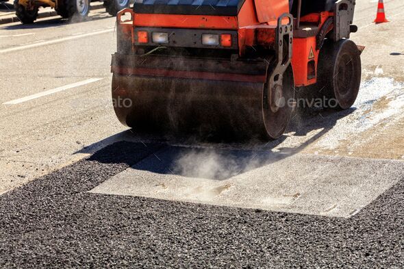 Heavy vibrating roller compacting hot asphalt on a repaired asphalt surface