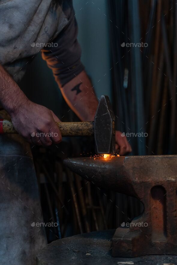 Vertical closeup of a blacksmith forging a tool by heating metal and working with hammer in a smithy