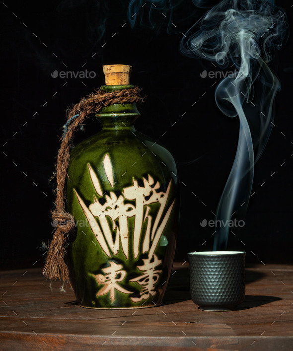 Closeup of a Japanese cultural sake jug and a small smoking cup on the side on a wooden table