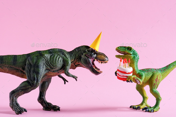 Cute happy green dinosaurs in birthday hats holding cake with flaming candles on pink background.