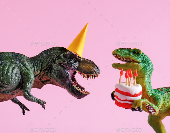 Cute happy green dinosaurs in birthday hats holding cake with flaming candles on pink background