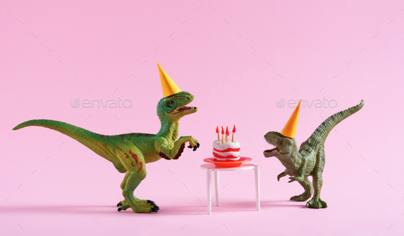 Cute happy green dinosaurs in birthday hats with cake with flaming candles on pink background.
