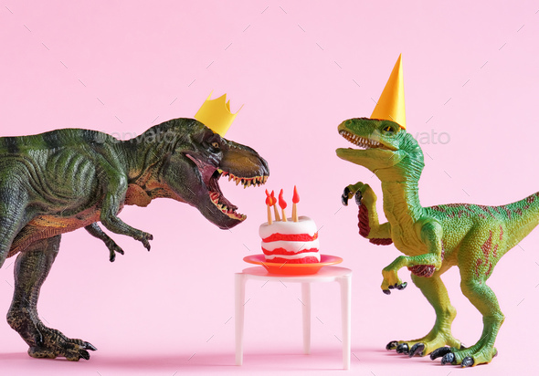 Cute happy green dinosaurs in birthday hats with cake with flaming candles on pink background.