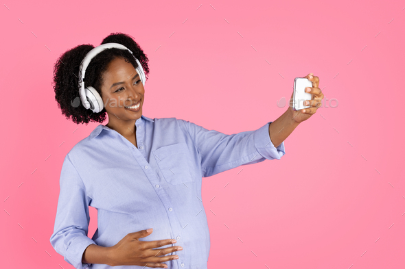 Happy millennial african american curly pregnant woman with belly in  headphones takes selfie on Stock Photo by Prostock-studio