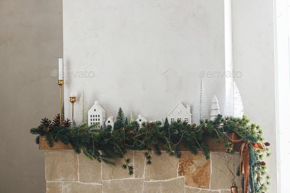 Modern christmas trees, houses, pine cones and spruce branches on fireplace mantel