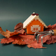 Dry maple leaves around a miniature orange house with a rake on a green background - PhotoDune Item for Sale