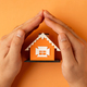 Hands covering a miniature orange house on a yellow background - PhotoDune Item for Sale