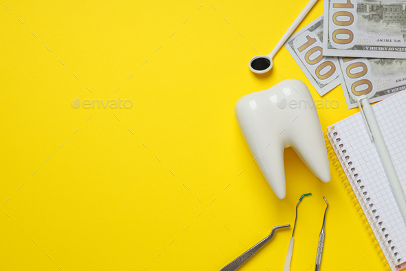 Dental tools, money, decorative tooth and notepad on yellow background, space for text