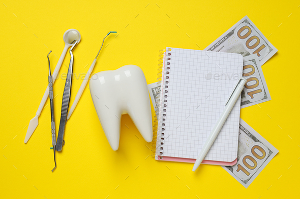 Dental tools, money, decorative tooth and notepad on yellow background, top view