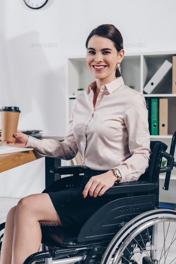 Disabled employee on wheelchair looking at camera and smiling with paper cup of coffee in office