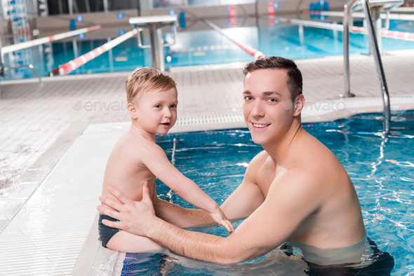 happy swim trainer and toddler kid near swimming pool