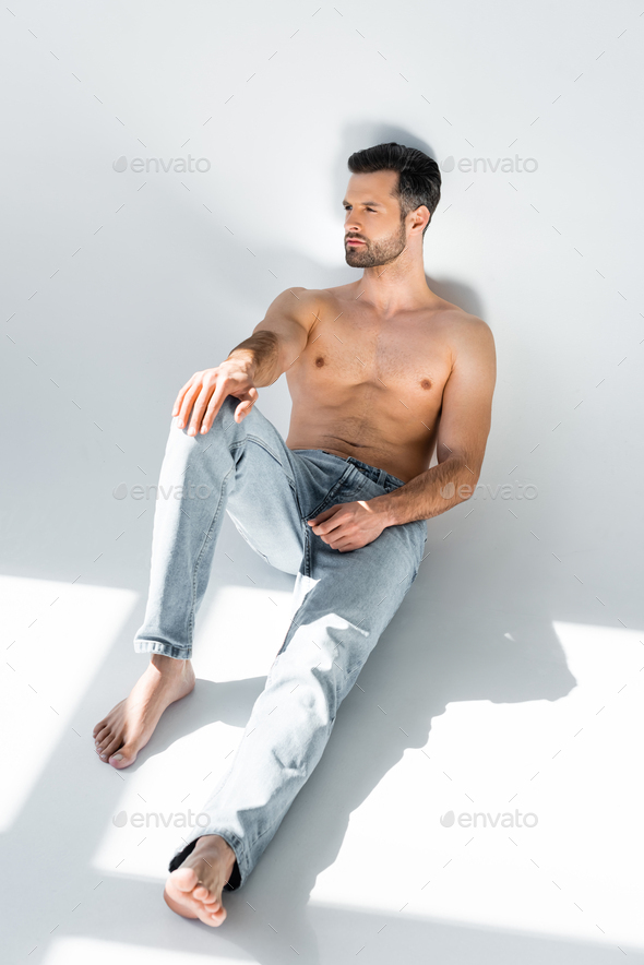 sunshine on muscular man in blue denim jeans sitting on grey Stock ...