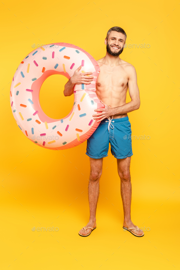 full length view of happy bearded guy with swim ring on yellow
