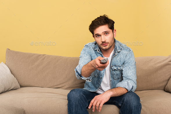 Handsome man holding remote controller while sitting on couch