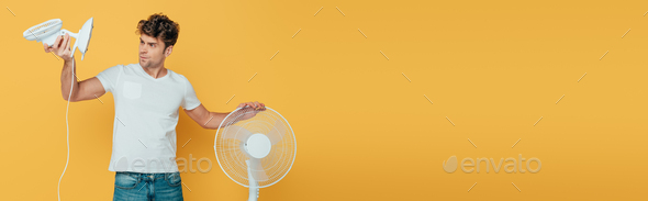 Concentrated and worried man looking at desk fan isolated on yellow, panoramic shot
