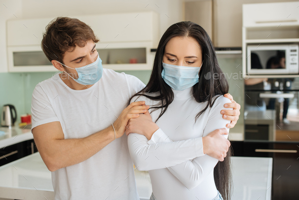 man hugging ill woman in medical mask at home during self isolation