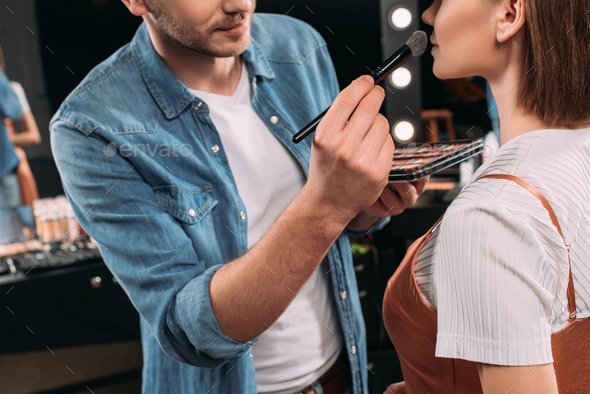 Cropped view of makeup artist applying blush on model in photo studio