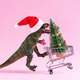 Happy green toy dinosaur carrying shopping cart with Christmas tree on pastel pink background. - PhotoDune Item for Sale