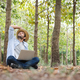A young man wearing a straw hat happily uses a notebook while working in the forest garden. - PhotoDune Item for Sale
