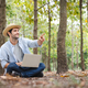 A young man wearing a straw hat happily uses a notebook while working in the forest garden. - PhotoDune Item for Sale