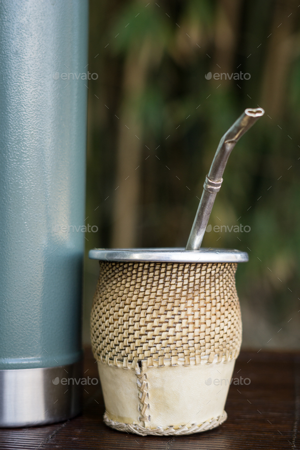 Vertical closeup of a cup of yerba mate infusion with a thermos. Stock  Photo by wirestock
