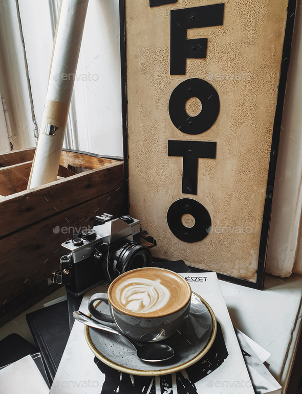Vertical shot of a cup of coffee and vintage camera on books and magazines on a window sill