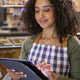 Smiling Young Woman Wearing Apron Working In Food Shop Using Digital Tablet - PhotoDune Item for Sale