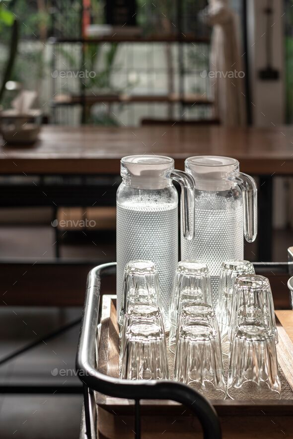 Vertical selective focus shot of glass water pitchers and empty upside-down  glasses on a tray Stock Photo by wirestock
