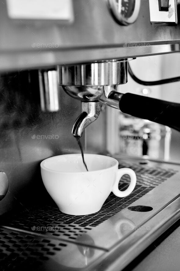 Vertical grayscale of coffee pouring from the coffee machine into a cup