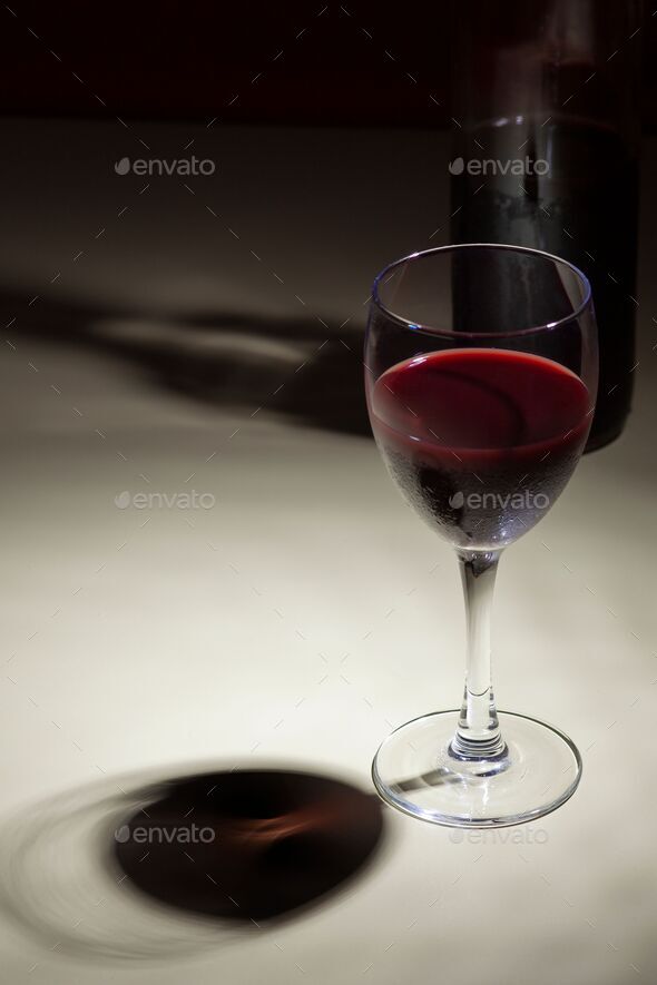 Bottle of red wine with a single glass of the same beverage, sitting side by side on a table.