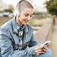 Shaved head girl using mobile smartphone while listening to music with headphones in the city street - PhotoDune Item for Sale
