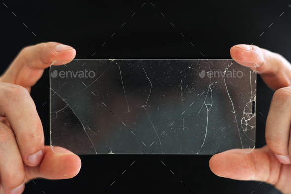 Broken protective glass for smartphone touch screen in hands of phone repairman on black background.