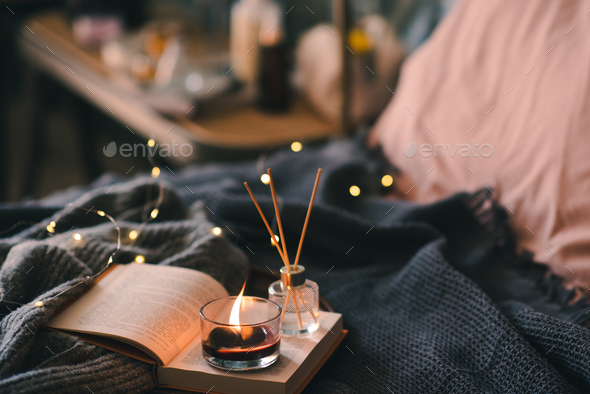 Cozy home atmosphere with candle and book in bed - Stock Photo - Images