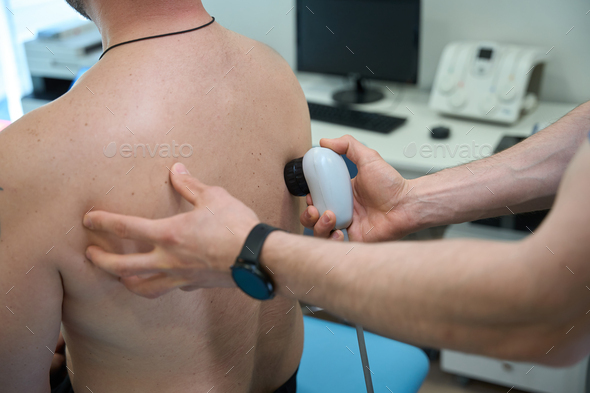 Physiotherapist treating patient for upper back pain with ultrasonic device  Stock Photo by svitlanah